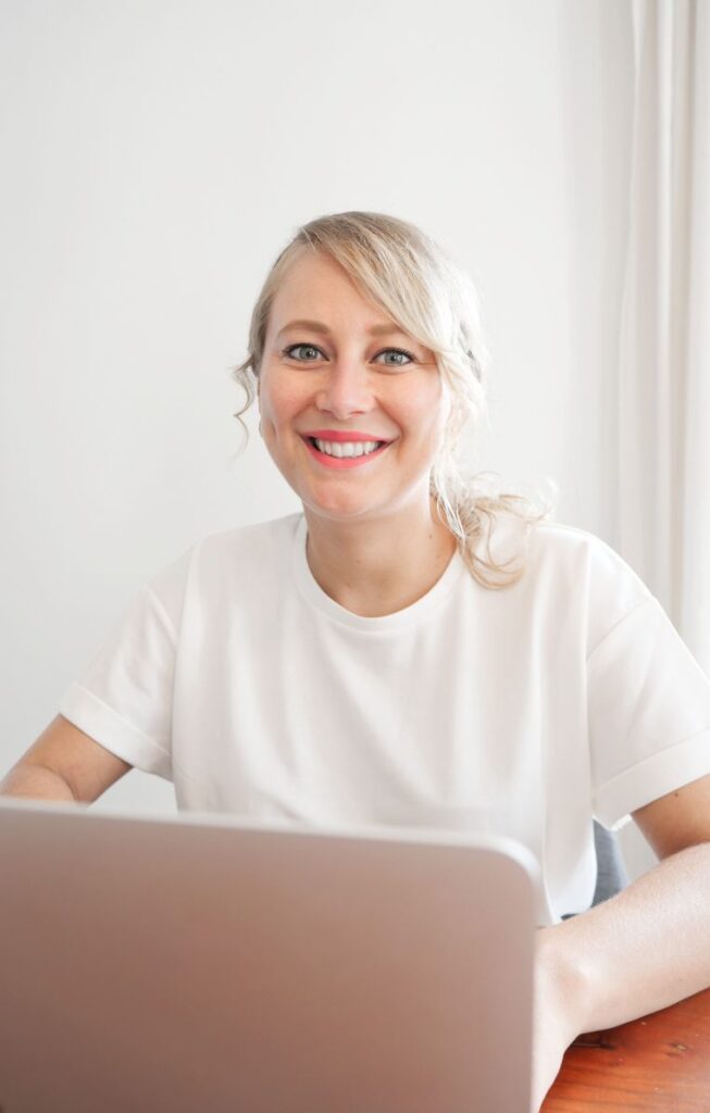 Ein Coach für Frauen sitzt an einem Holztisch und lächelt in die Kamera