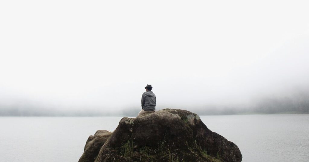 Mein wahres Ich: So findest du zurück zu dir 3 Ein Mann sitzt alleine auf einem Stein und schaut in die Ferne